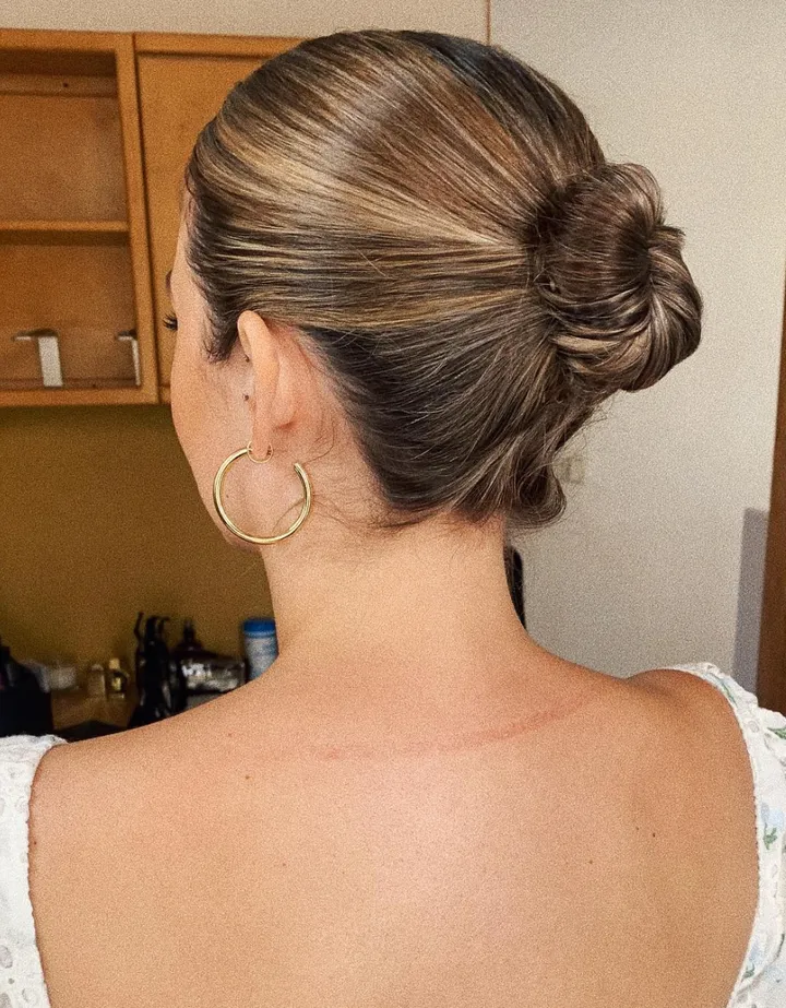 A bride with her hair styled in a sleek, slicked-back, elegant bun, wearing large gold hoop earrings.