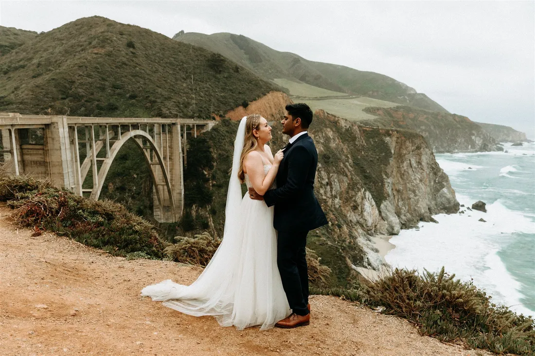 Bride and groom embrace on a bluff overlooking Bixby Creek Bridge in Big Sur