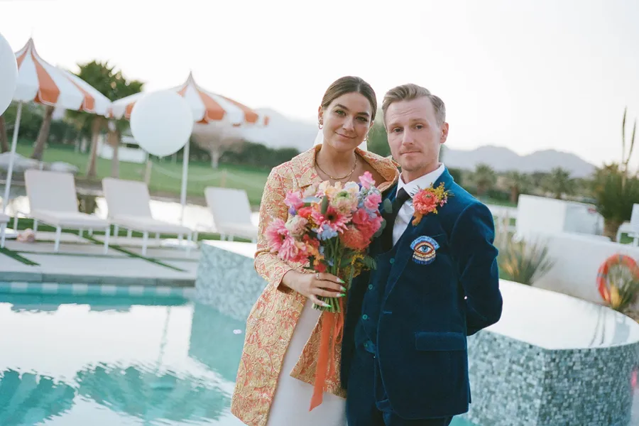 Bride and groom pose in front of iconic looking pool at their palm springs estate wedding venue