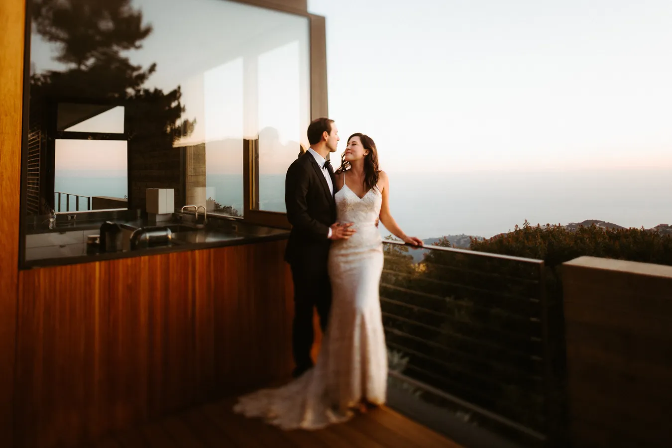 A bride and groom standing close together on a balcony, gazing into each other's eyes duri