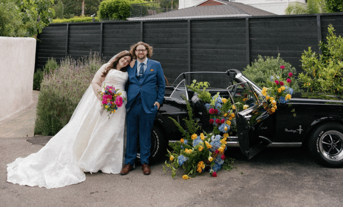 bride and groom pose in front of classic convertible covered in colorful florals