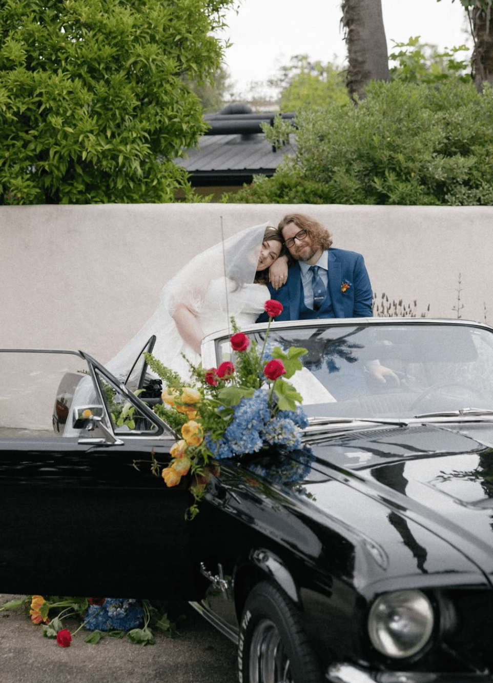 bride and groom pose in front of classic convertible covered in colorful florals