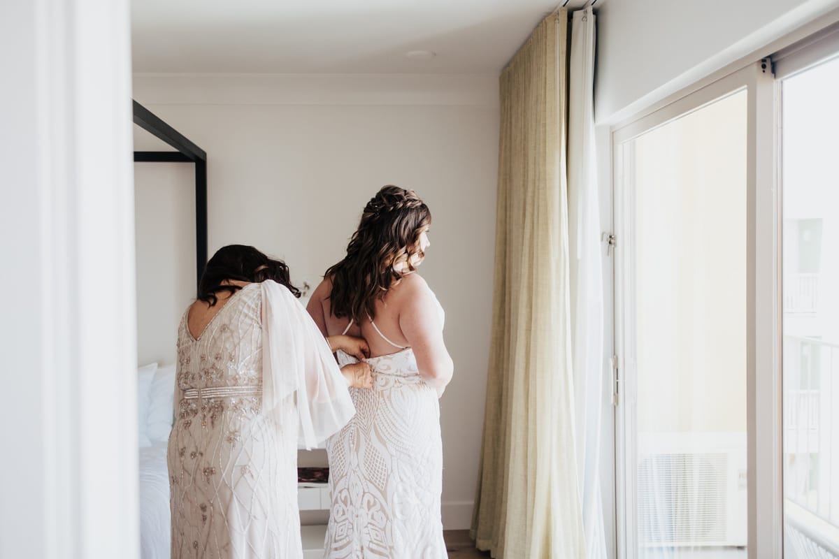mom of the bride getting the bride into her wedding gown