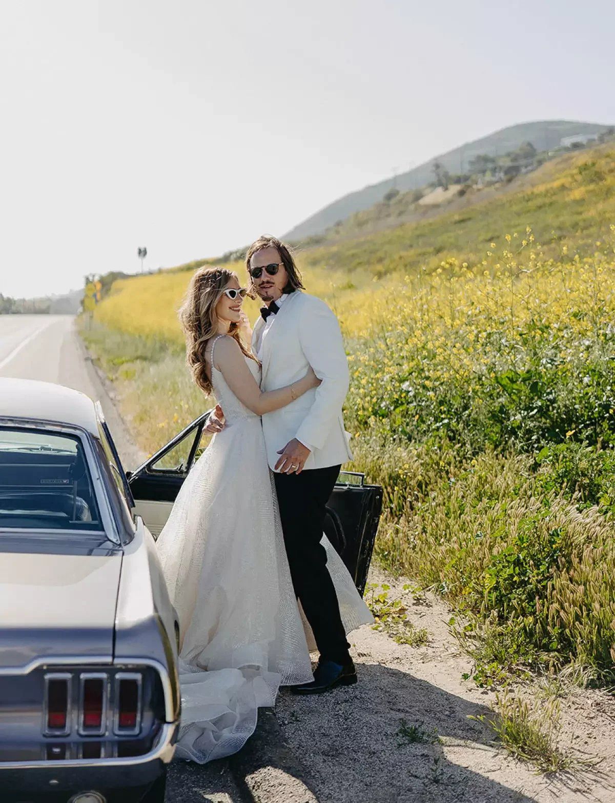bride poses with mustang in malibu on her wedding day, surrounded by blooming yellow flowers
