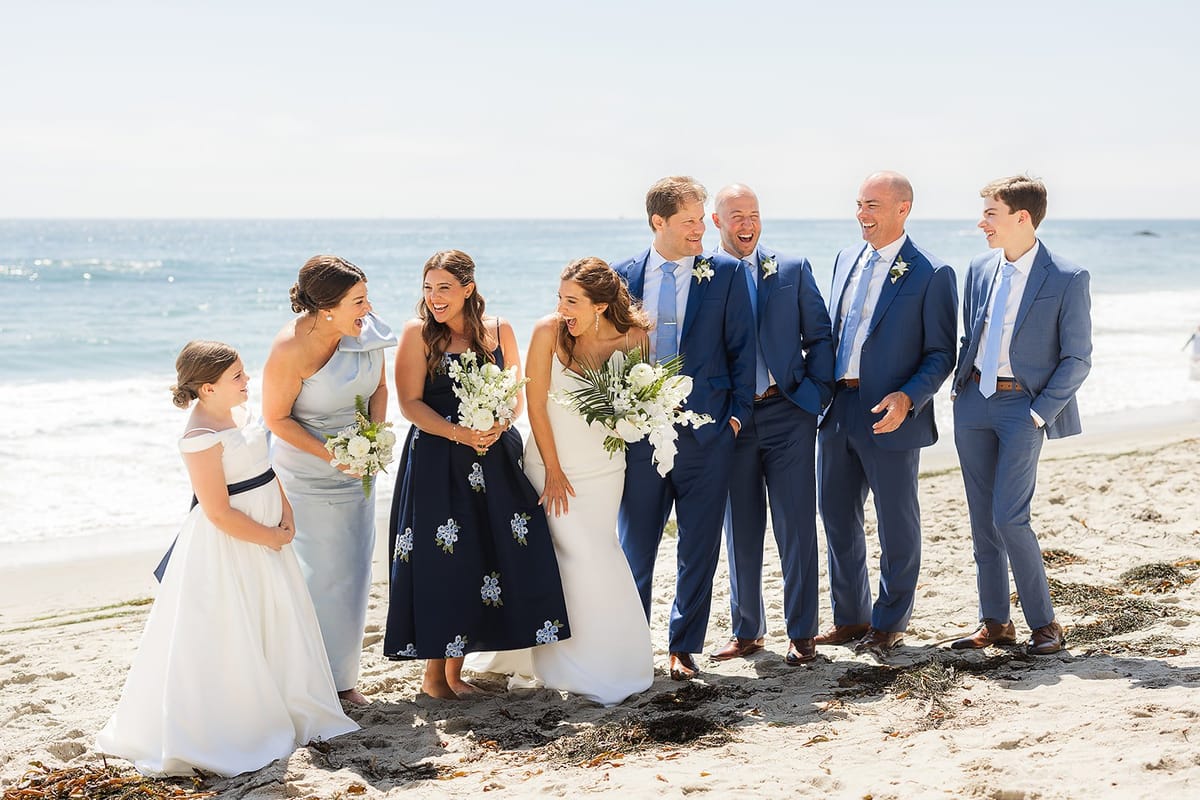 bridal party in blue pose for photos on the sand in laguna beach