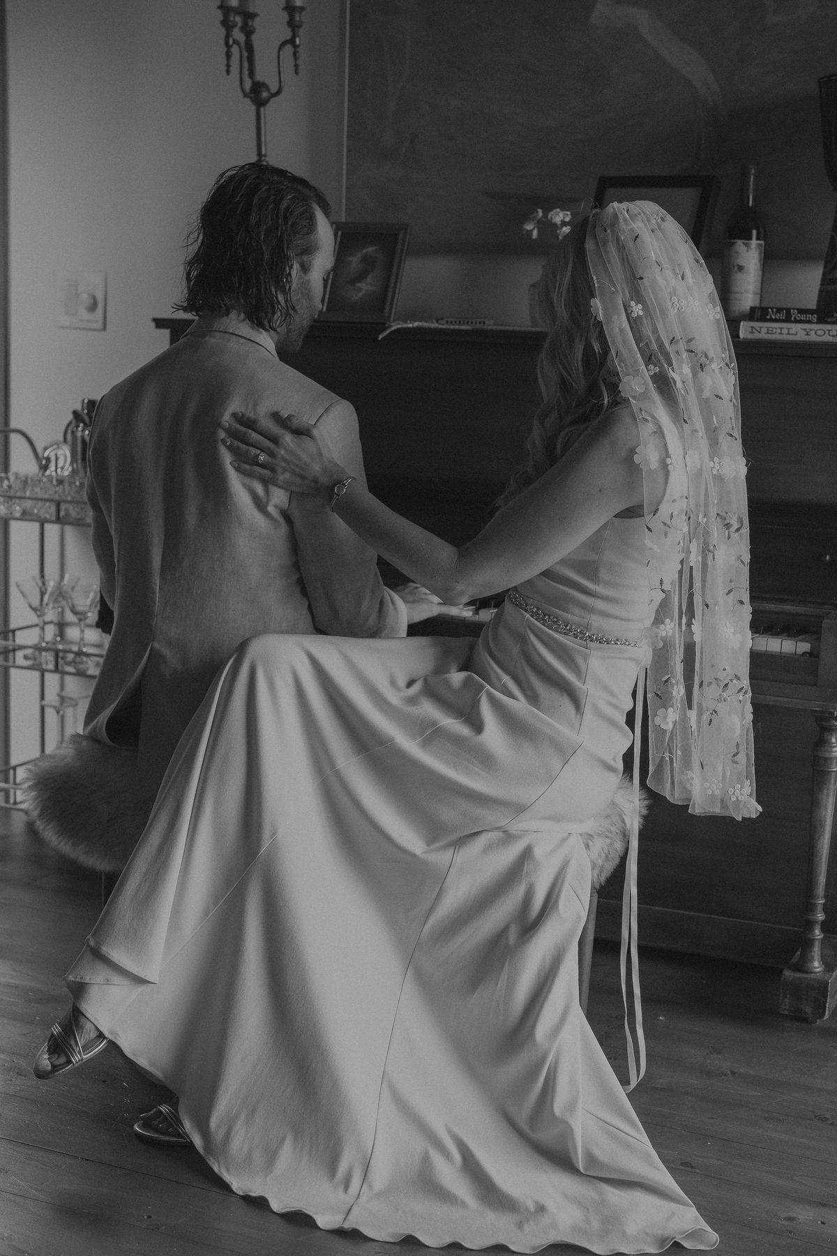 bride and groom sit at the piano together before their southern california wedding
