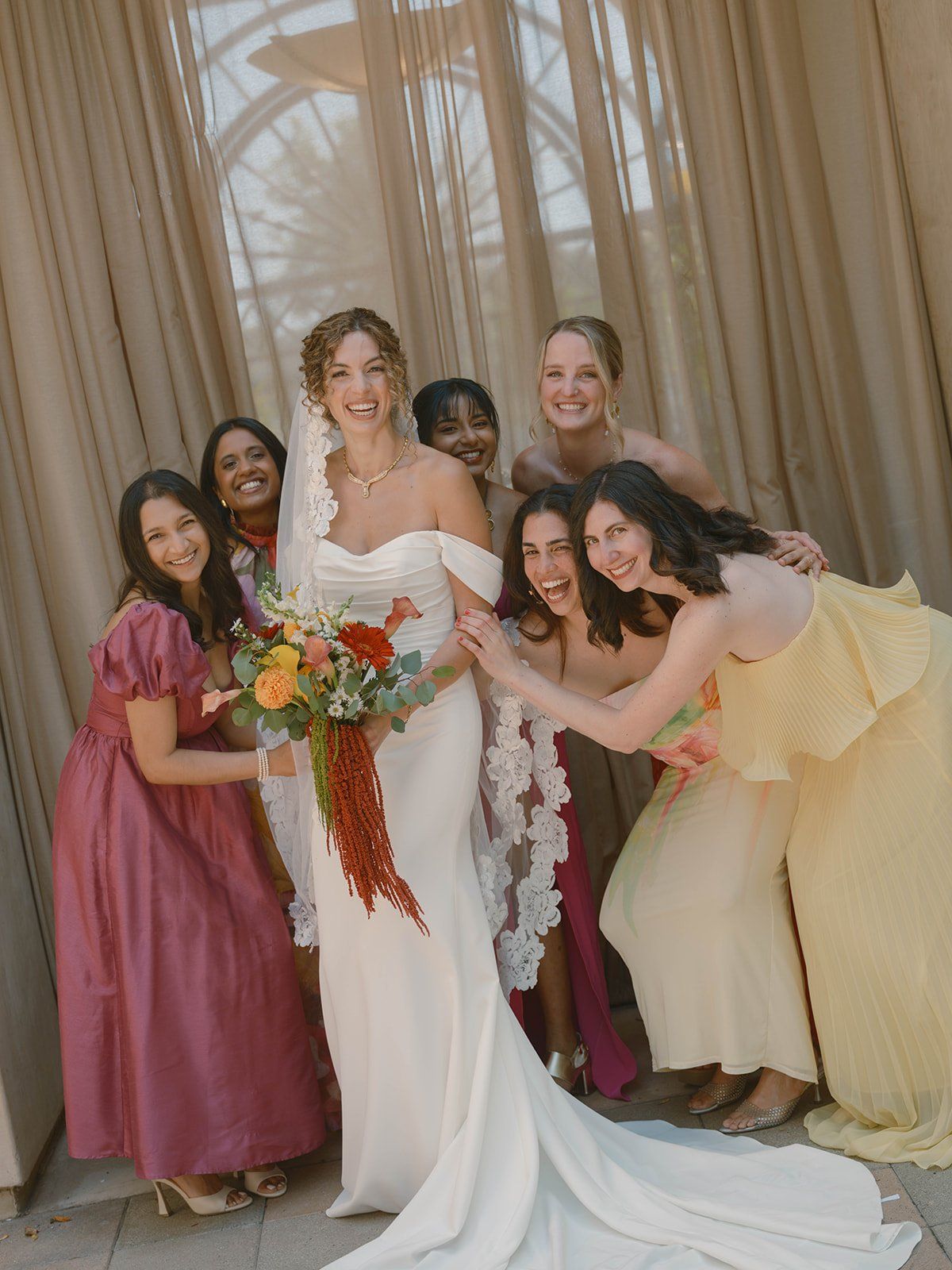 bride and her bridal party on the wedding day in san juan capistrano. Bridal party is dressed in colorful, vibrant dresses.