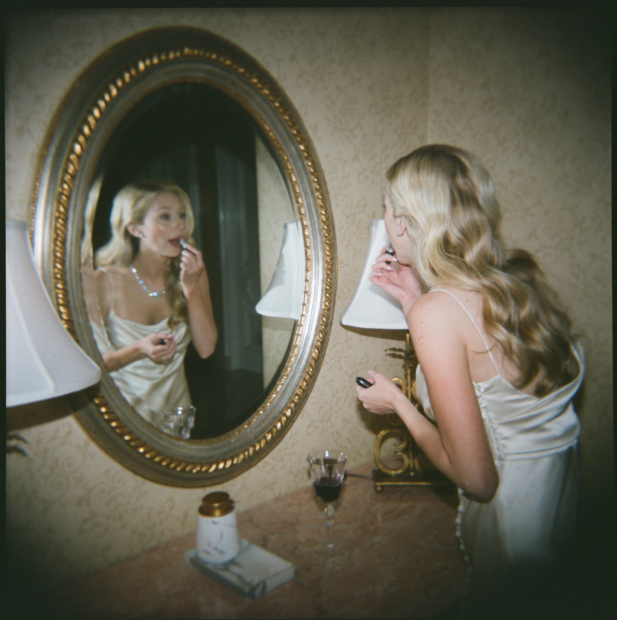 beverly hills bride applies a lipstick touch up in front of mirror on her wedding day morning